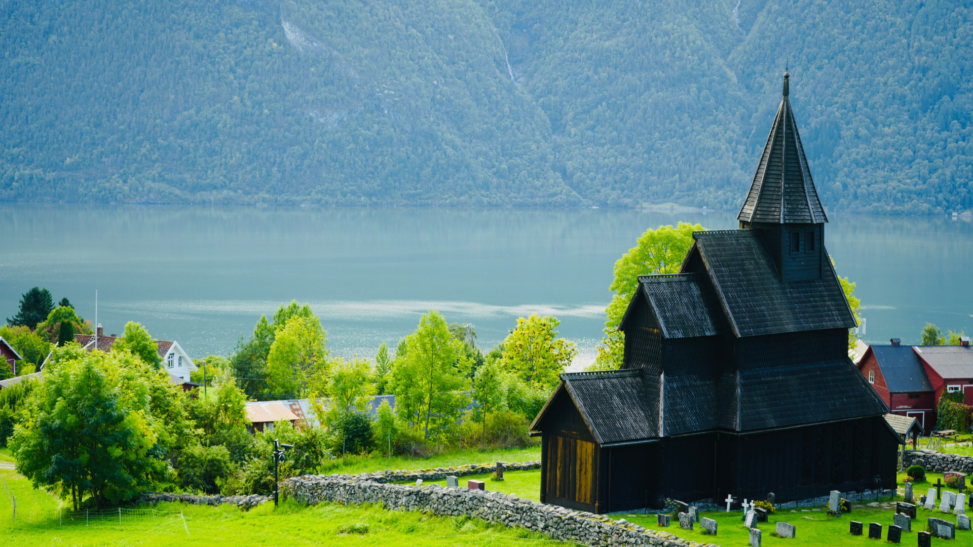 Urnes_Stave_Church The historic Urnes Stave Church in Norway. This remarkable wooden church, a UNESCO World Heritage Site, features intricate carvings and a distinctive architectural style from the 12th century. The church's dark wood contrasts with the lush greenery surrounding it.