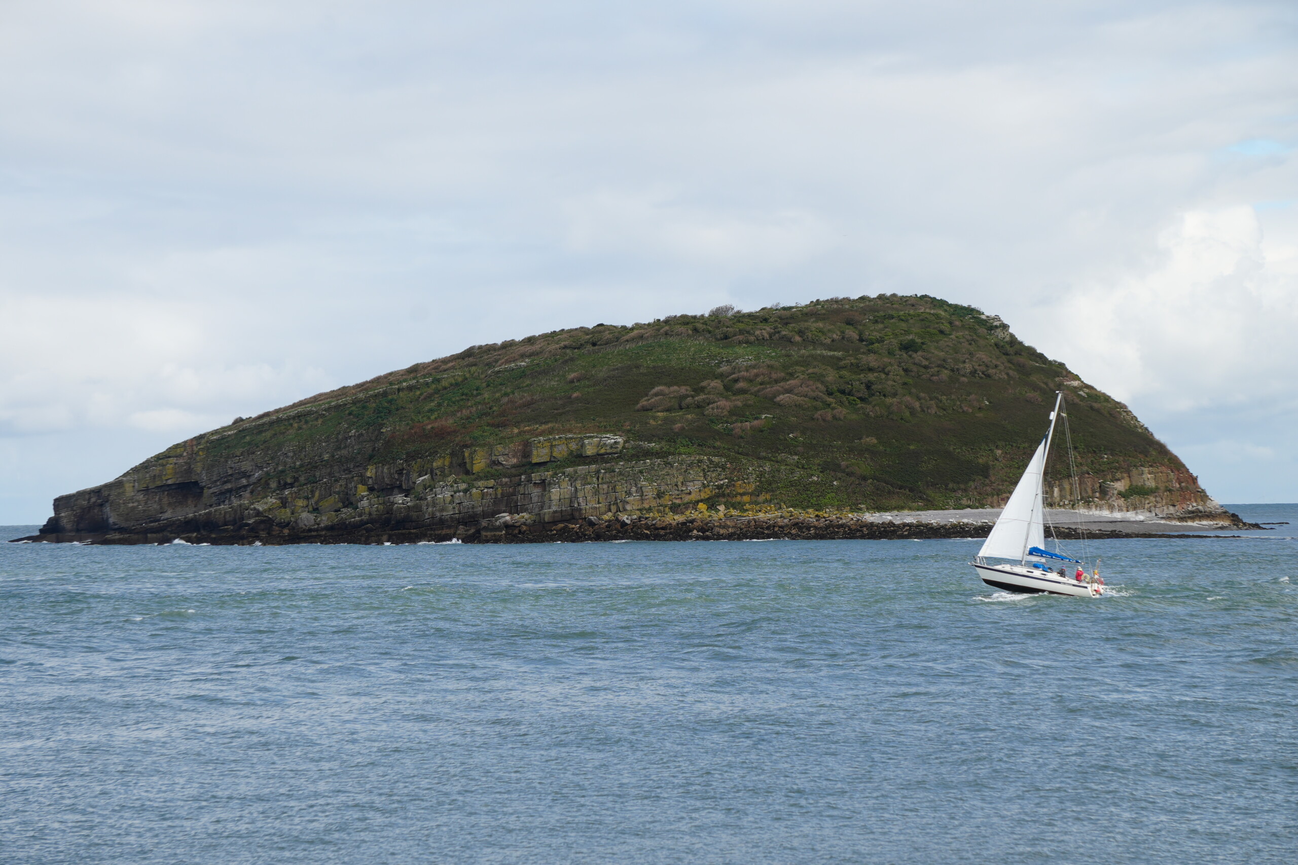 Puffin_Island Puffin Island off the coast of Anglesey, with a sailboat in the foreground gliding across the calm waters on a partly cloudy day.