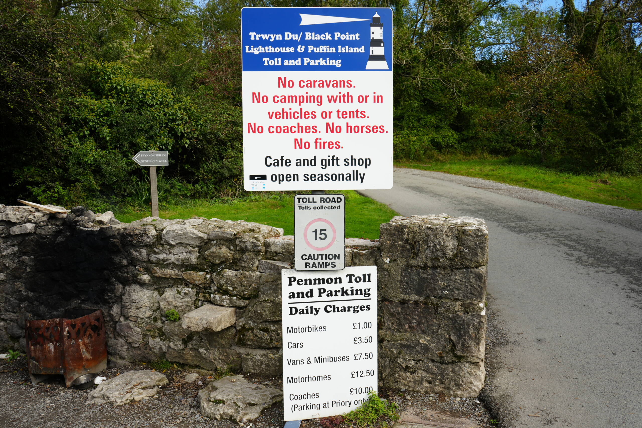 Toll_Road_Prices_Penmon_Point Sign at Penmon Point toll road detailing daily parking charges for vehicles, including motorbikes, cars, vans, motorhomes, and coaches, alongside rules prohibiting caravans, camping, and fires, with a note about the seasonal café and gift shop.